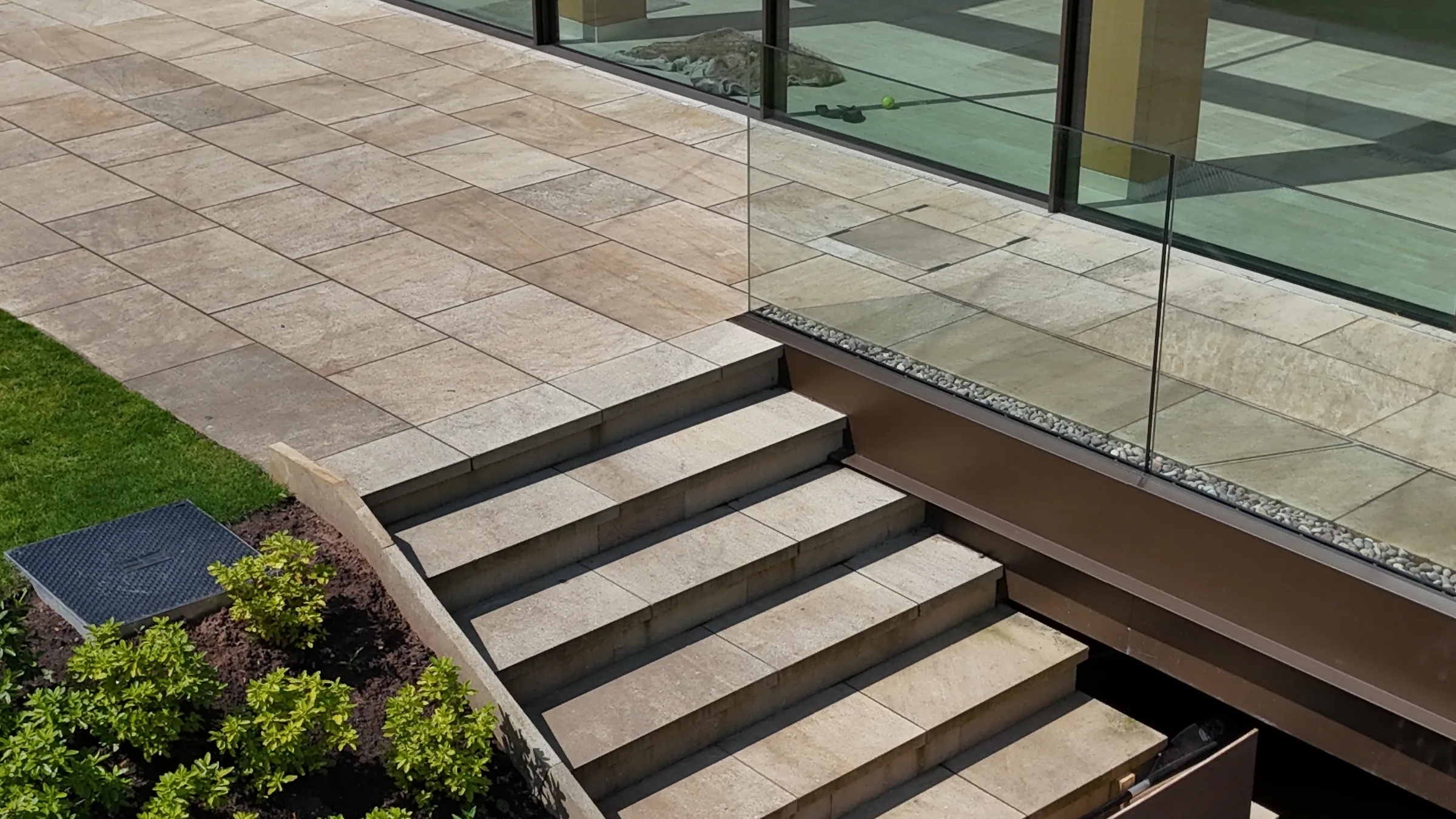 A set of stone steps leading up to a patio area with a glass balustrade, adjacent to a modern building.