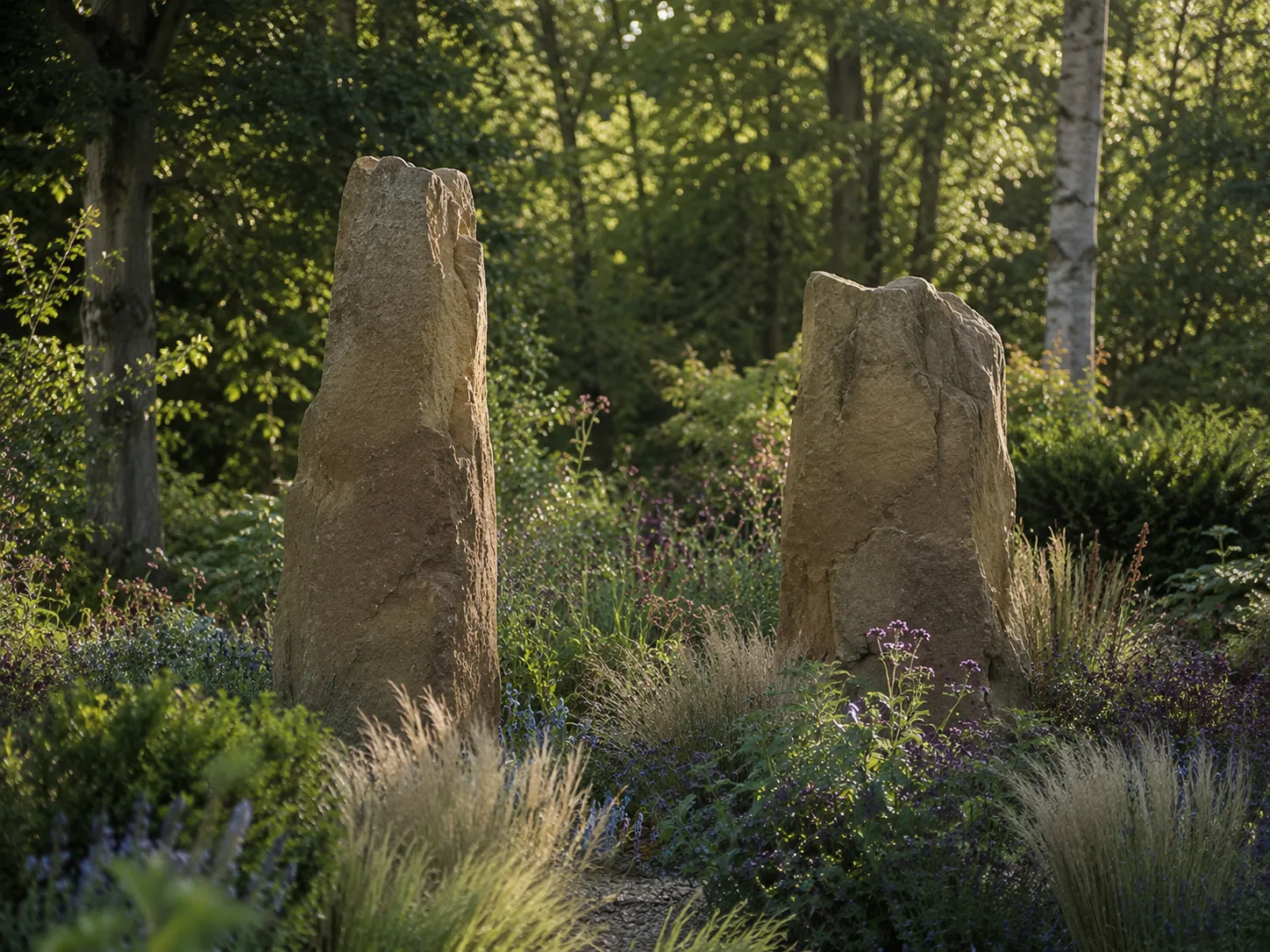 Two large standing stones surrounded by lush greenery in a woodland setting.